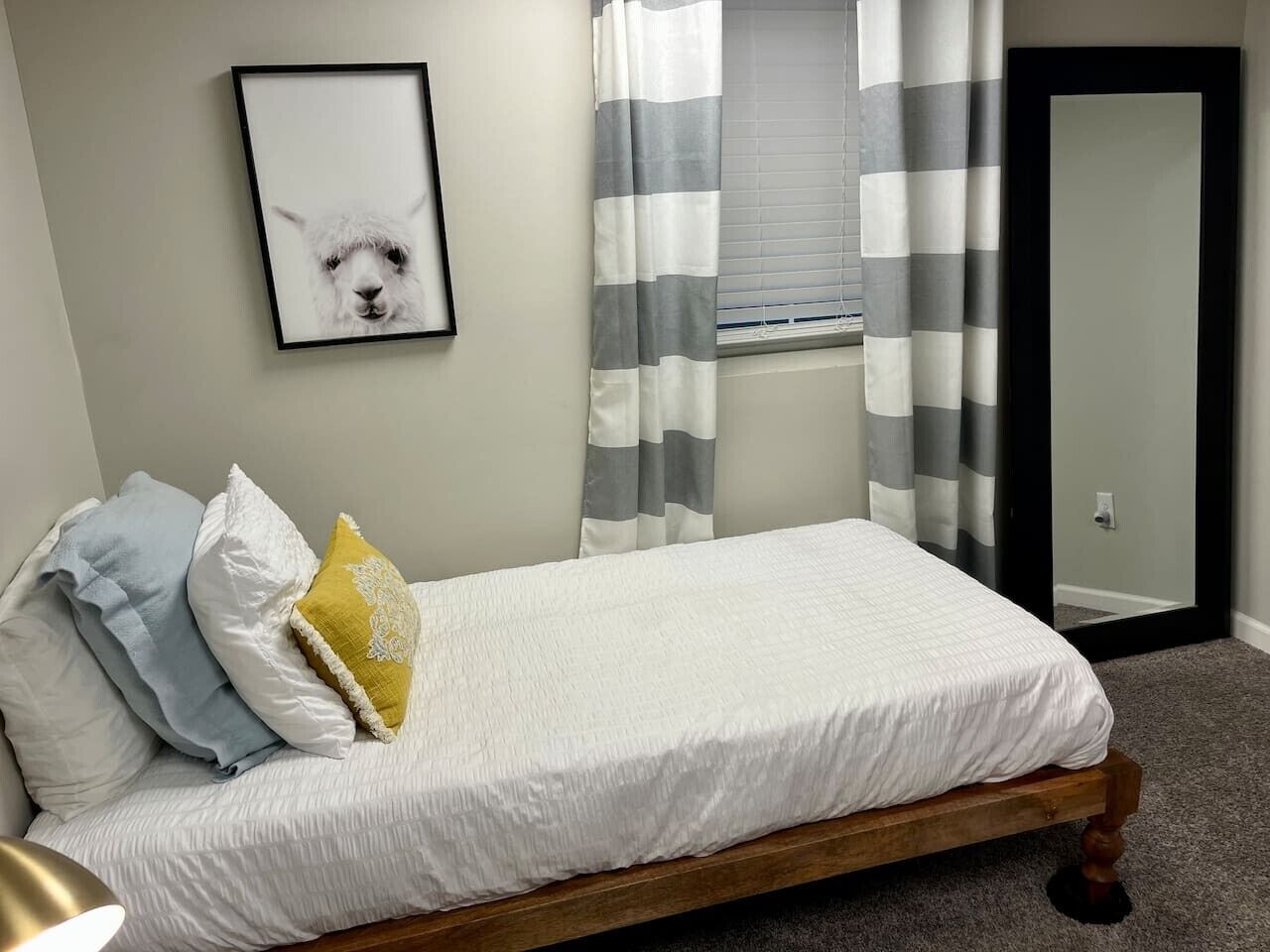 A single bed with a wooden frame, white bedding, and a framed picture on the wall.