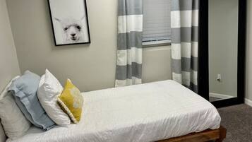 A single bed with a wooden frame, white bedding, and a framed picture on the wall.
