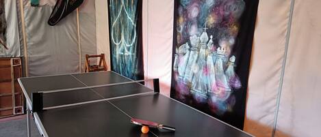 Una mesa de ping pong con una paleta de tenis de mesa, una silla de madera y una pared con un cuadro con temática de galaxia.