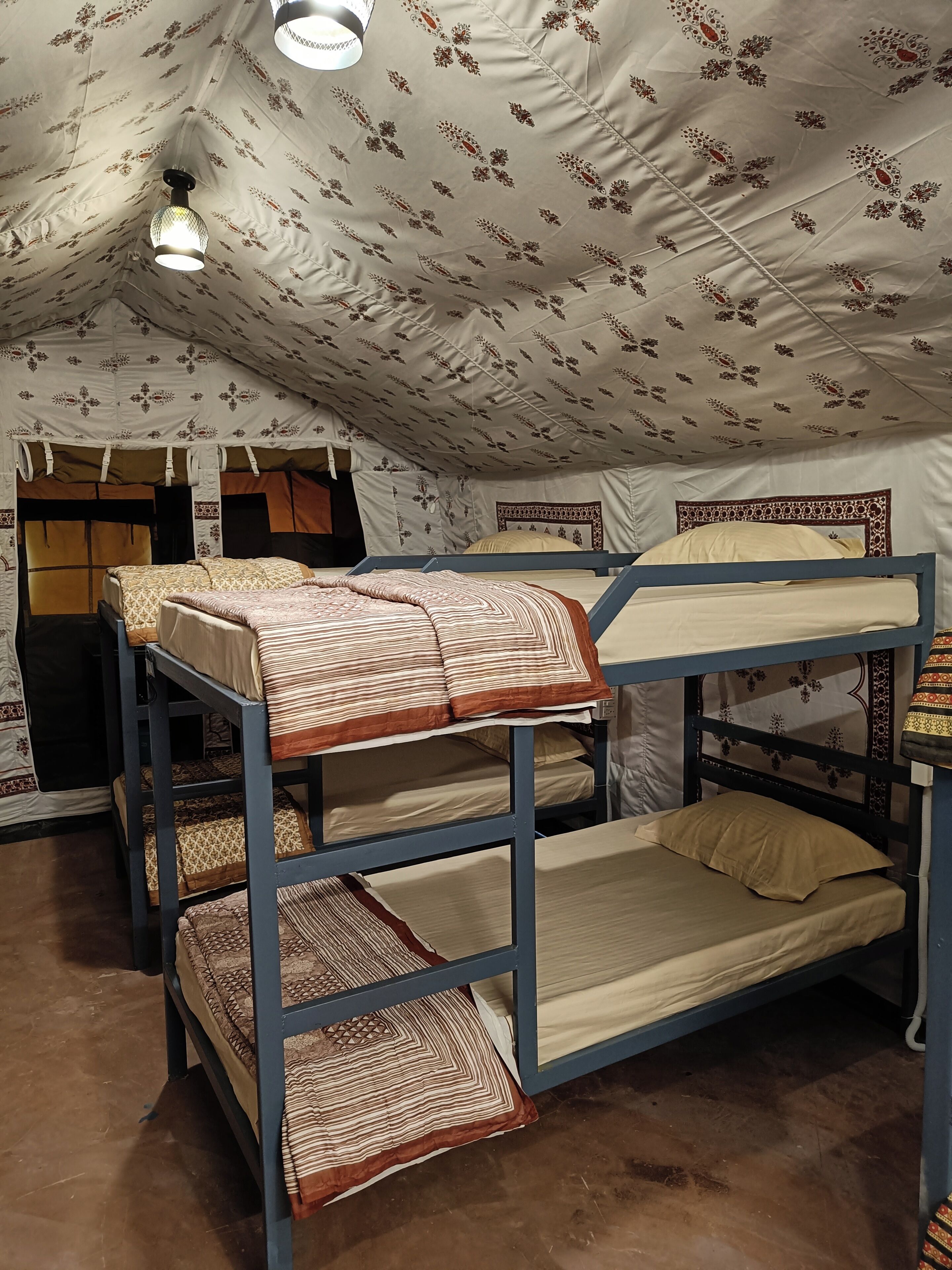 A dormitory-style room with bunk beds, patterned ceiling, and a hanging light fixture.