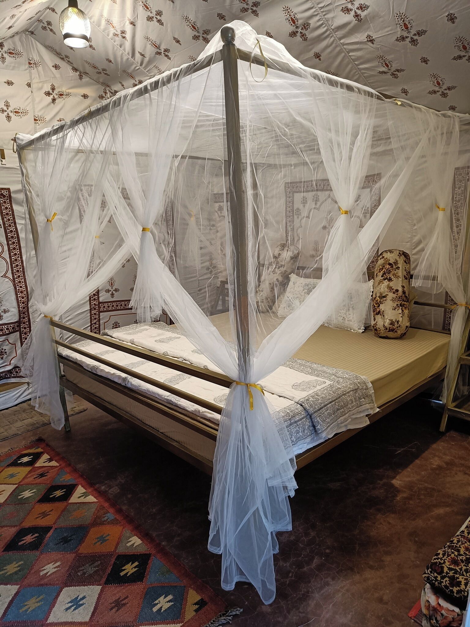 Una cama con dosel y cuatro columnas, con cubrecama blanco y almohada decorativa.