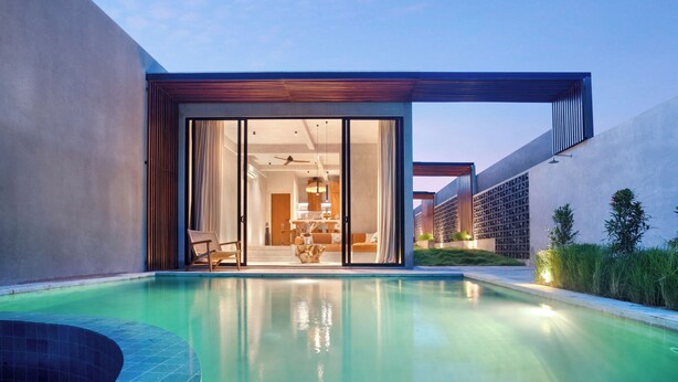 A modern poolside area with a clear view of the pool, a sliding glass door entrance to a room, and a building with a unique facade. - Garden Villa Ubud By BREIG (Ubud)