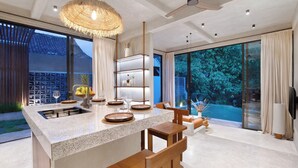 A modern kitchen with a central island, wooden chairs, and a large window overlooking a swimming pool. - Garden Villa Ubud By BREIG (Ubud)