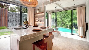 A modern kitchen with a large island, built-in shelves, and a view of a swimming pool. - Garden Villa Ubud By BREIG (Ubud)