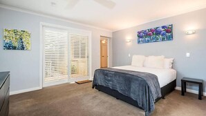 A bedroom with a bed, a ceiling fan, a door with blinds, and a painting on the wall.