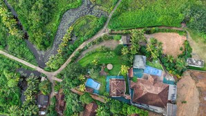 Vue aérienne d’une propriété comprenant une piscine, un court de tennis et une grande maison à toiture de chaume.