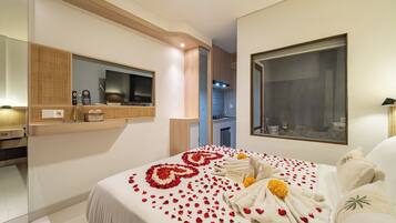 A hotel room with a bed adorned with rose petals and a welcome mat, a large mirror, and a view of the kitchen.