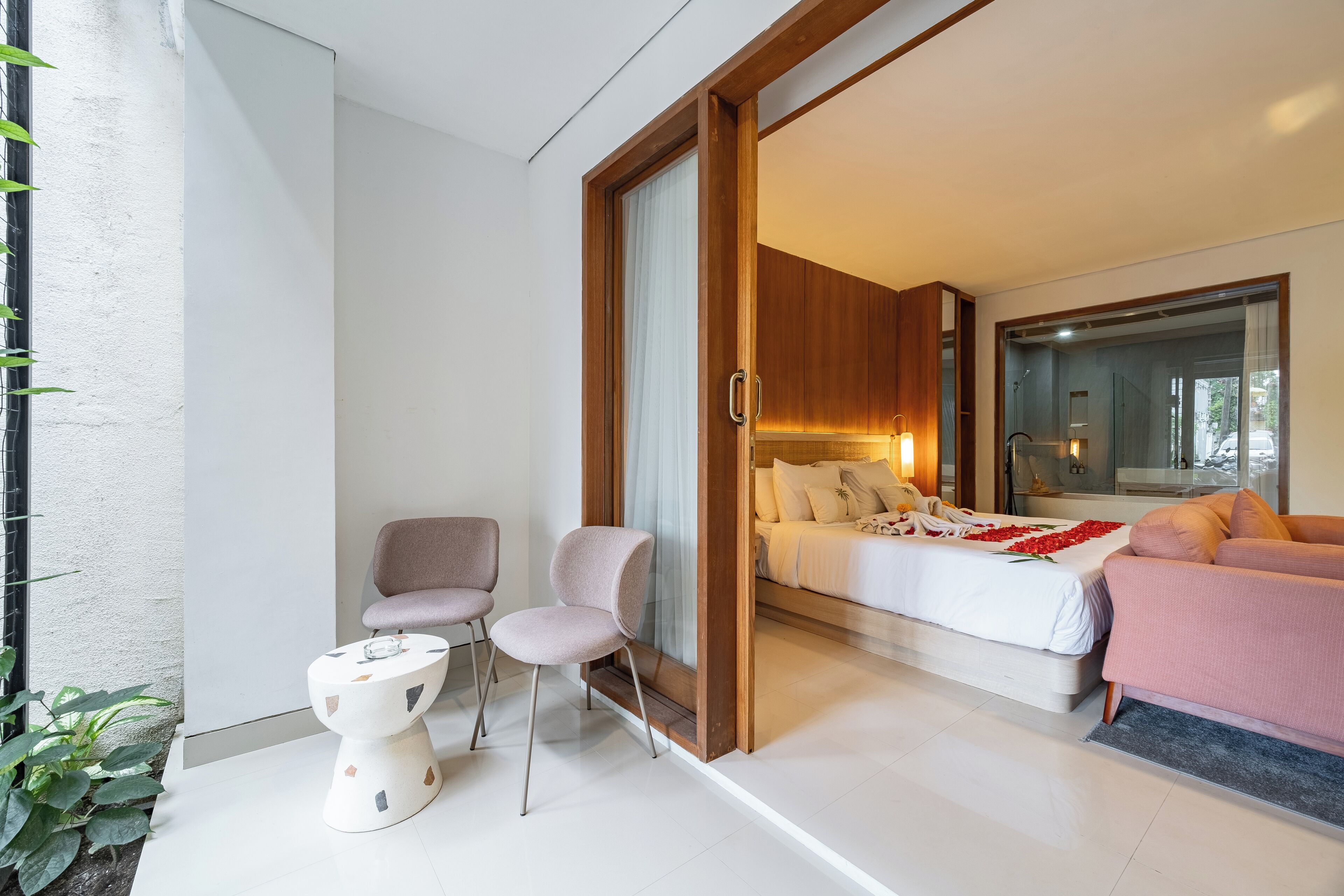 A modern bedroom with a bed, two chairs, a small table, and a large window.