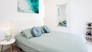 Quarto moderno com cama, luminária de cabeceira, espelho e uma obra de arte na parede.