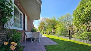 Een terras met buitenmeubilair, een bakstenen gebouw en een verzorgd gazon.