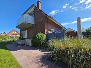 A two-story house with a balcony, a patio with outdoor furniture, and a fenced garden area.