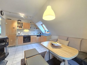 A compact kitchen with wooden cabinets, a dining area with a bench, and a loft bedroom with a bed and a window.