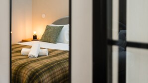 Un lit bien fait, avec une couverture à carreaux, un oreiller vert et une serviette blanche pliée posée sur le lit.