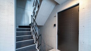 A modern staircase with a metal railing leading to a dark wooden door. - ALTIPLANO (Sapporo)