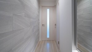 A modern hallway with light-colored walls and wooden flooring, leading to a door with a vertical window. - ALTIPLANO (Sapporo)