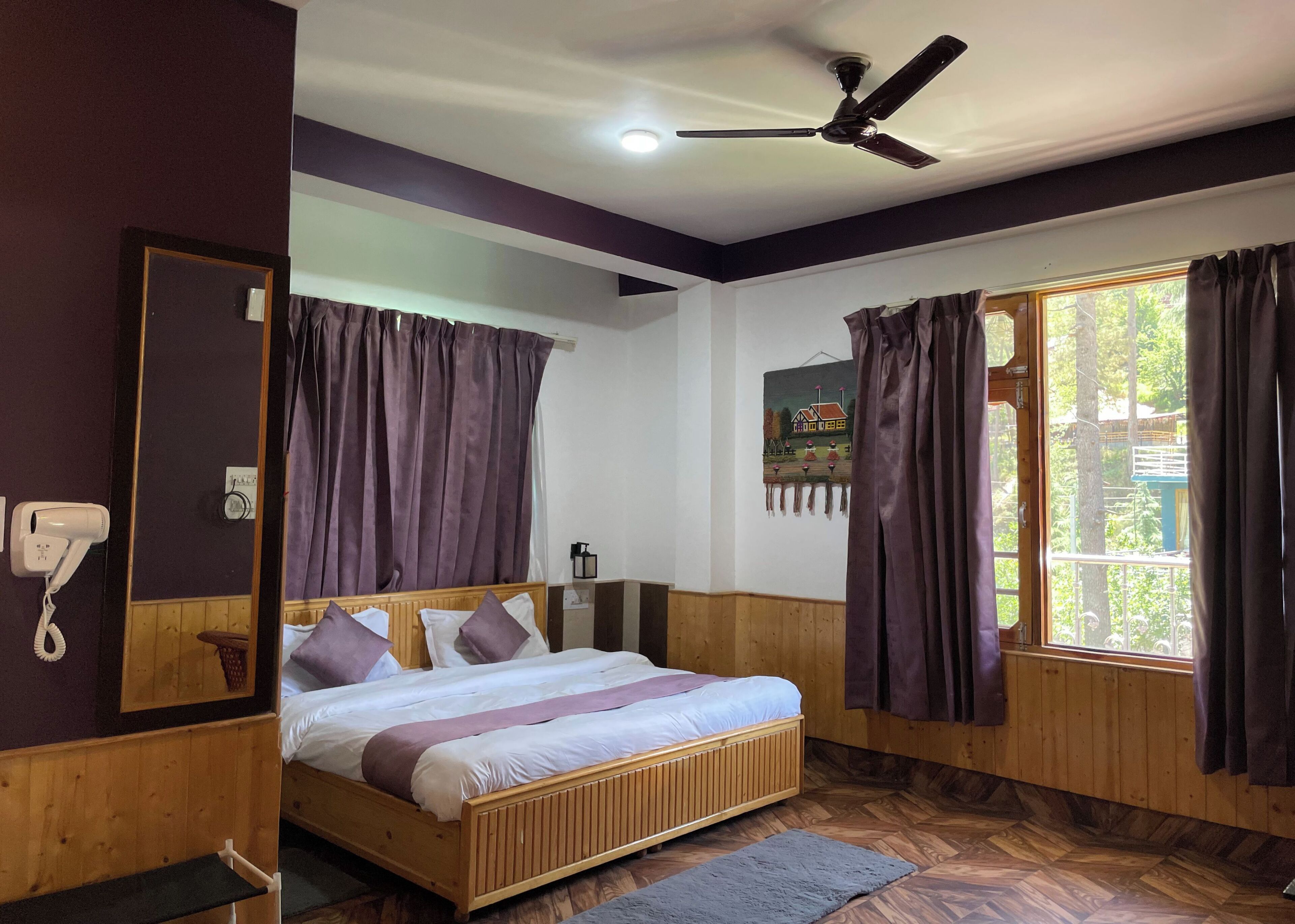 Une chambre à coucher avec un lit en bois, des rideaux violets, un ventilateur de plafond et une fenêtre donnant sur un paysage verdoyant.
