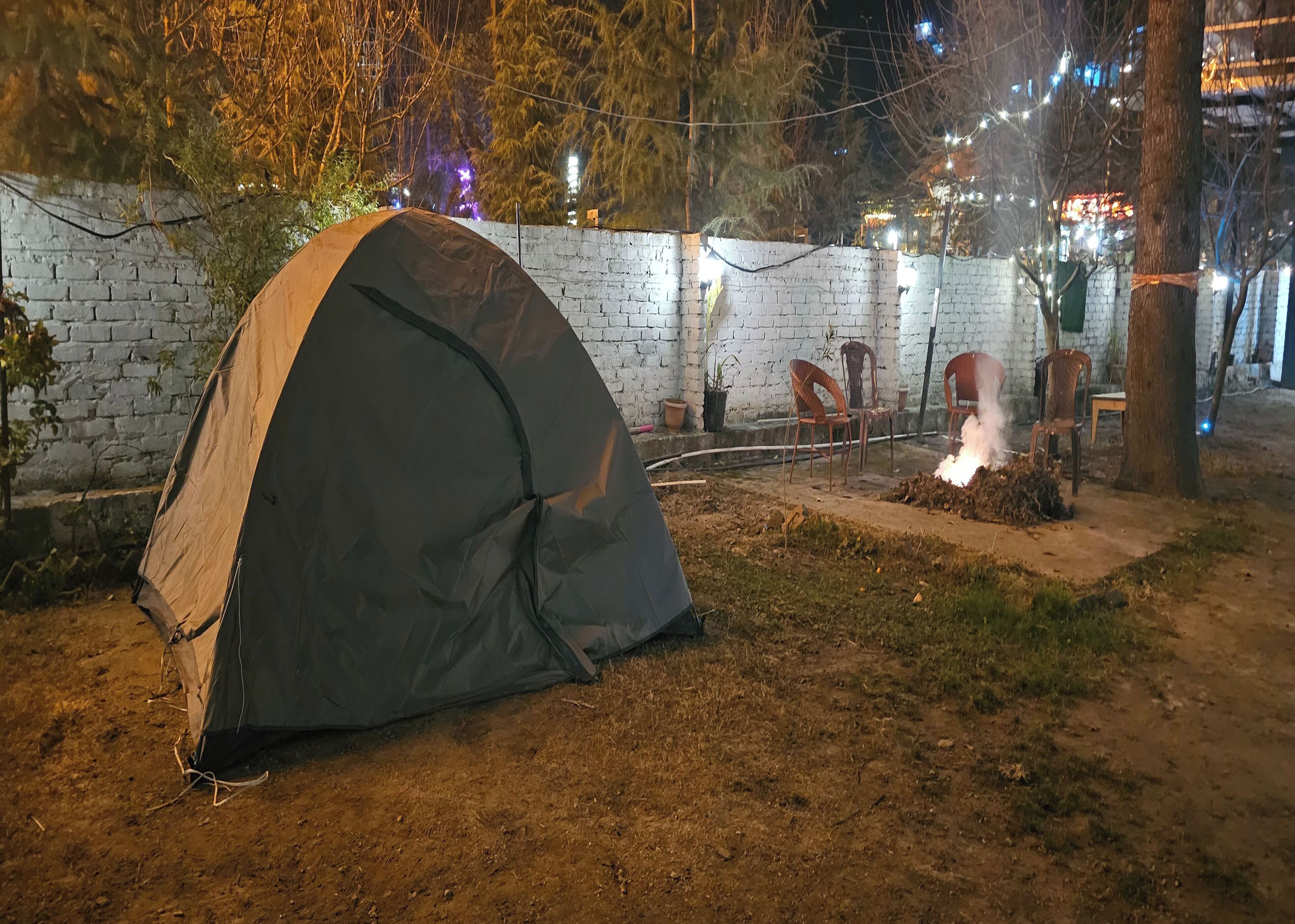 Tenda montada em área externa, com parede de tijolos, cadeiras e lareira.