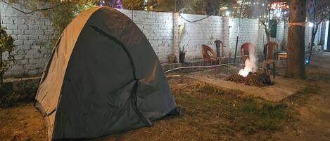 Tenda montada em área externa, com parede de tijolos, cadeiras e lareira.