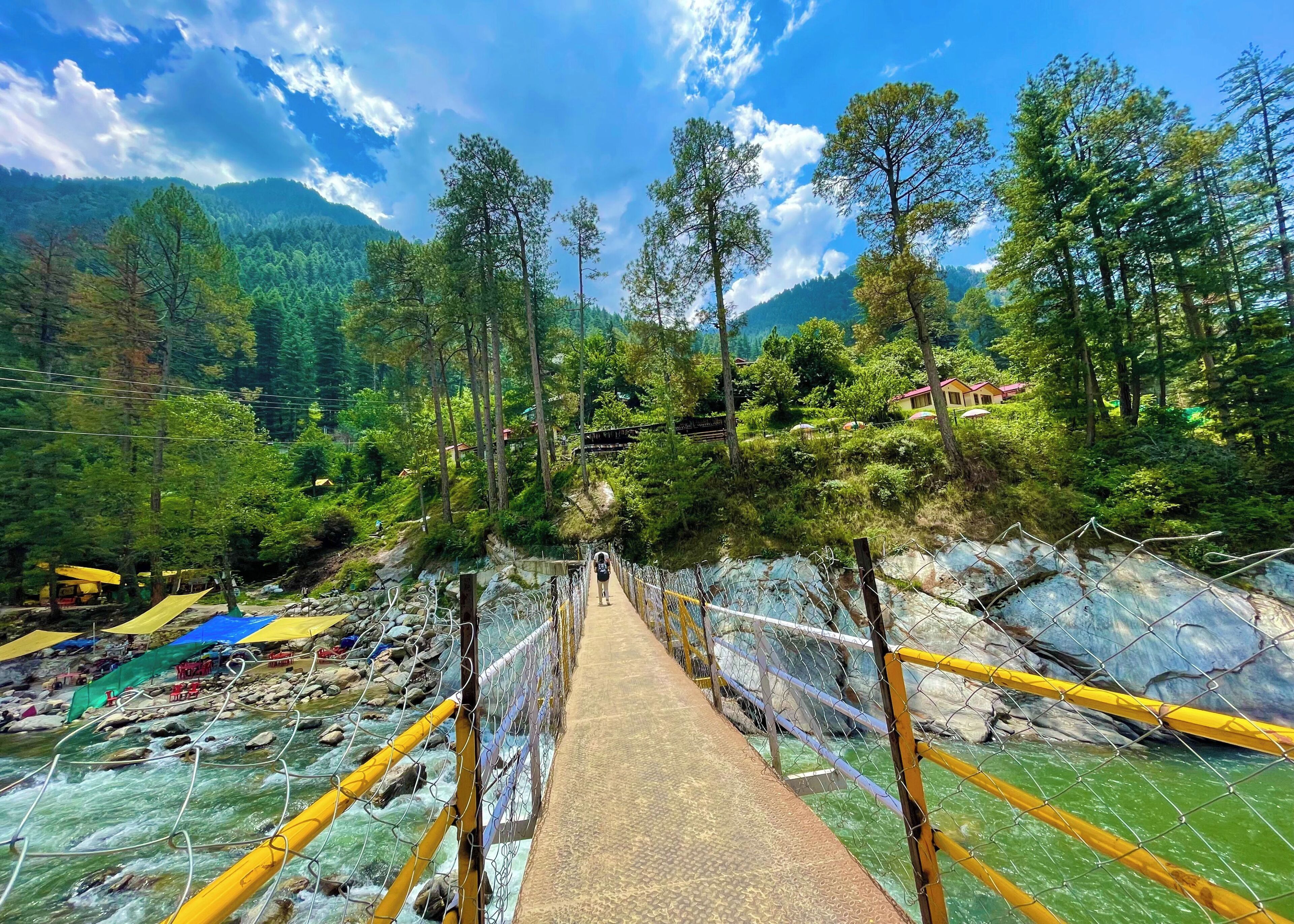 Un puente colgante sobre un río, con una montaña boscosa al fondo.
