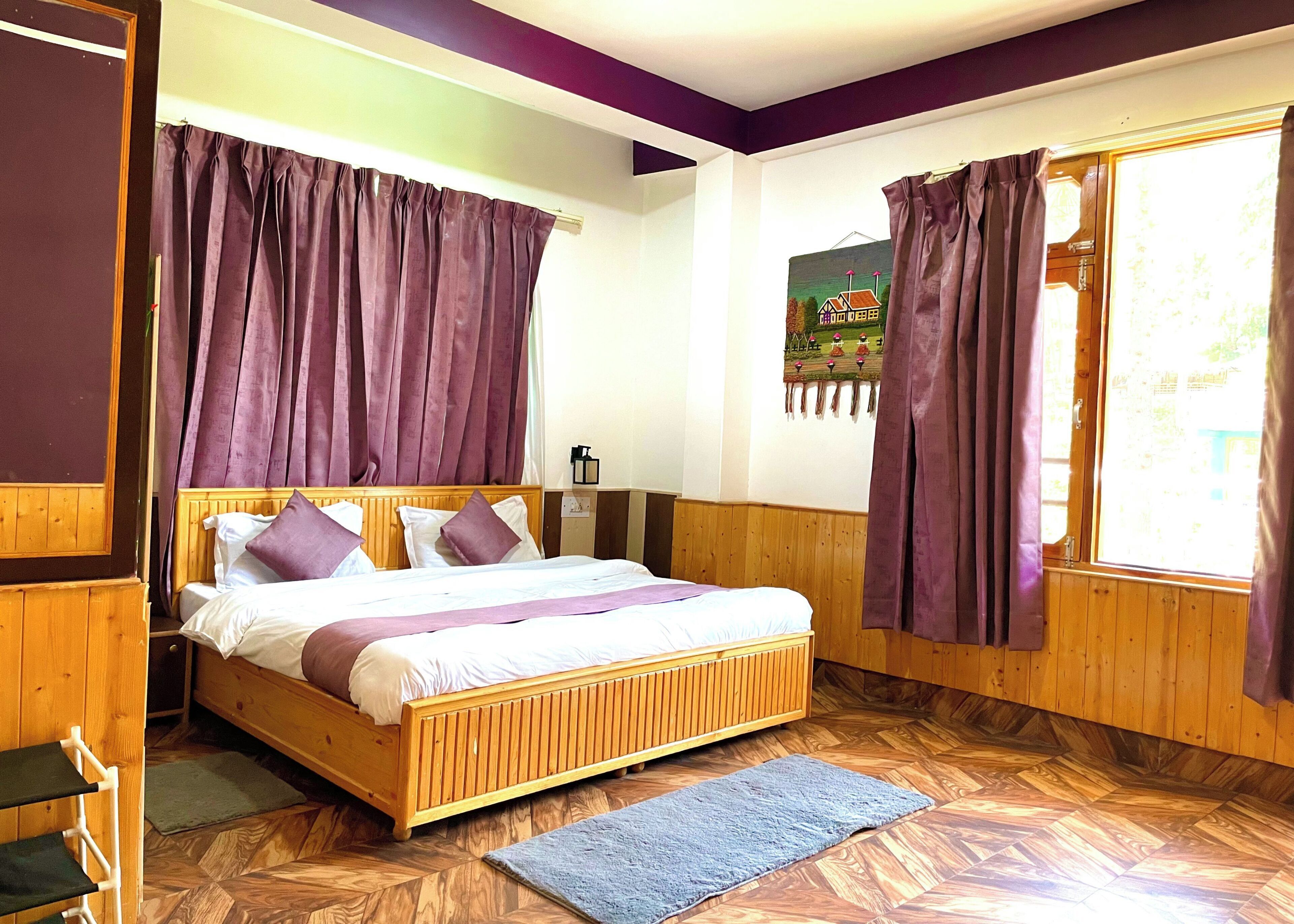 Una cama con estructura de madera, cabecera, cortinas moradas y una alfombra azul sobre un piso con estampado de greca.