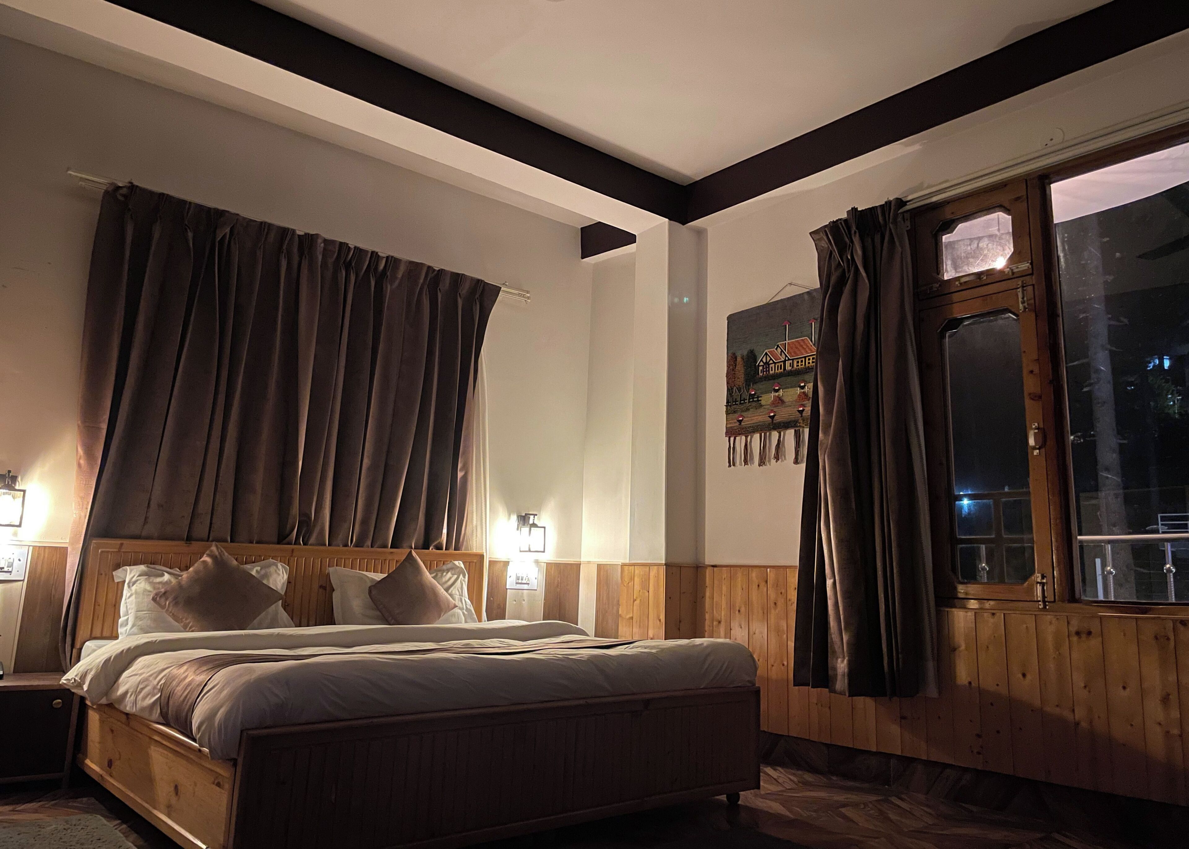 A bedroom with a wooden bed, two bedside lamps, a window with curtains, and a wall-mounted painting.