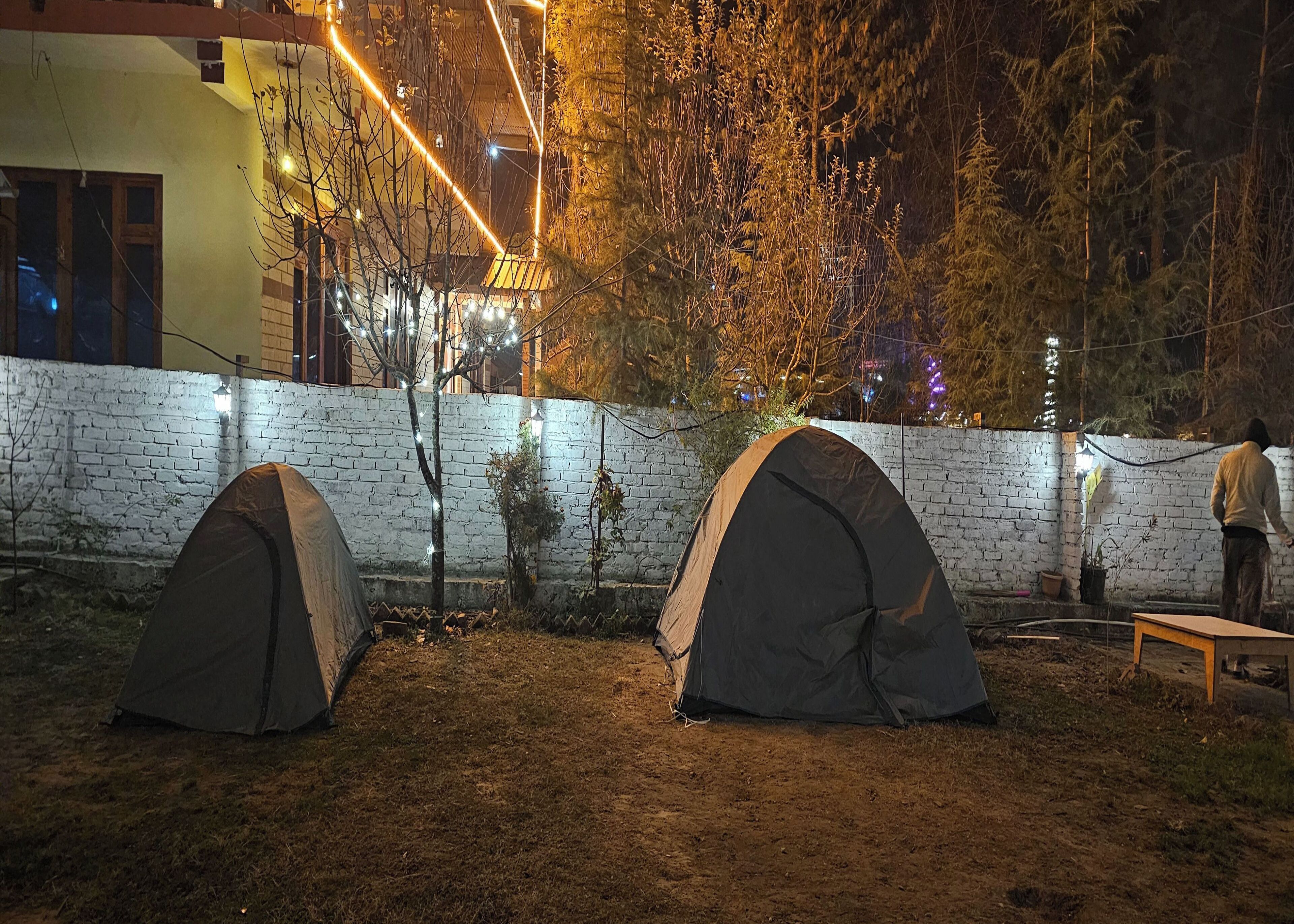 Two tents set up in an outdoor area with a brick wall and string lights.