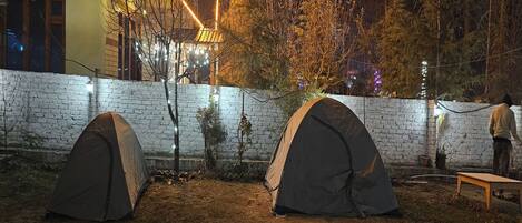 Two tents set up in an outdoor area with a brick wall and string lights.