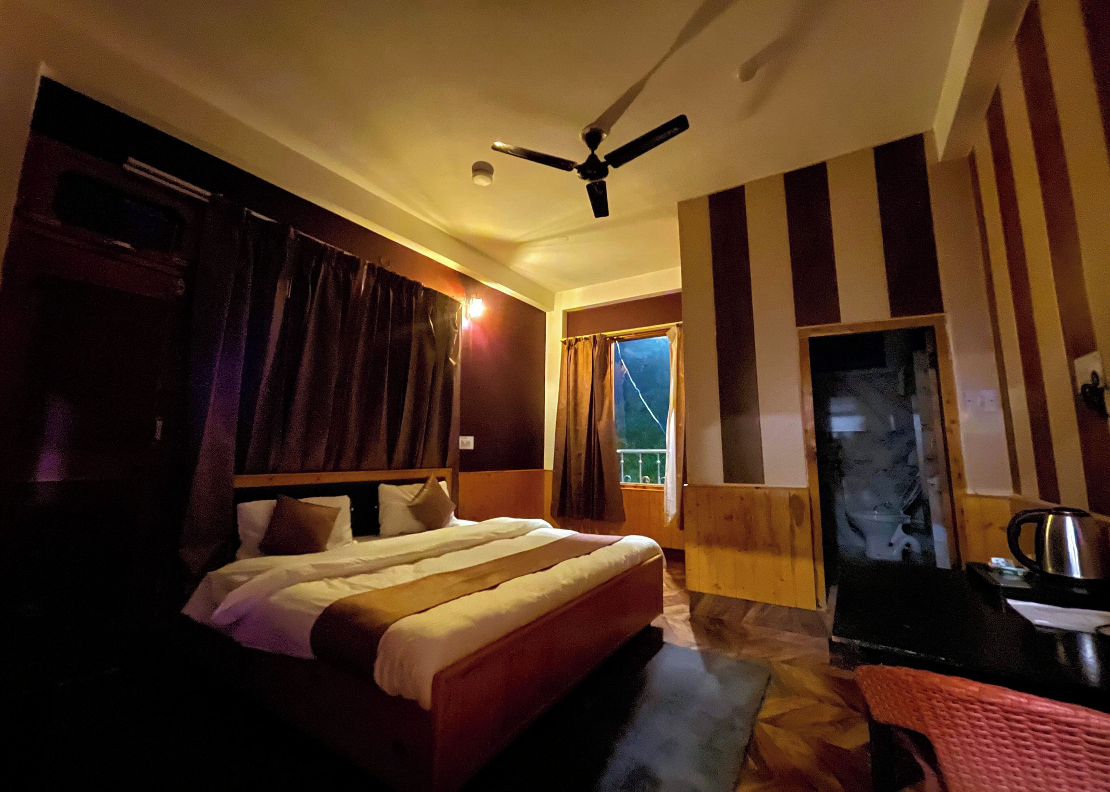 Hotelkamer met een bed, een plafondventilator, een raam met gordijnen en uitzicht.
