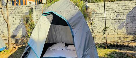 Une tente avec un espace aménagé pour dormir, installée contre un mur de pierre et bordée d’arbres.
