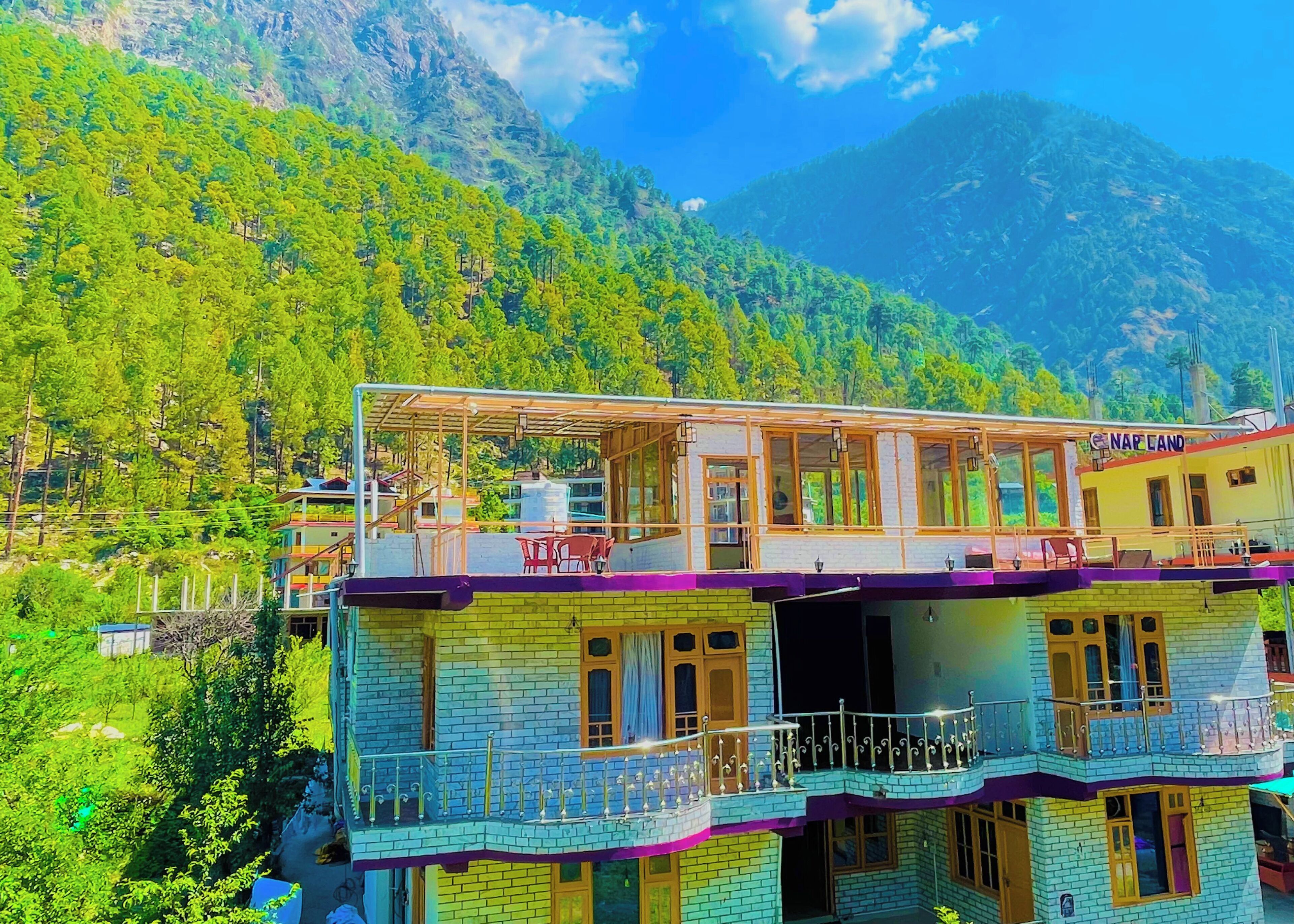 Un edificio de varios pisos con balcones, un letrero que dice "NAP LANDS" y un paisaje montañoso de fondo.