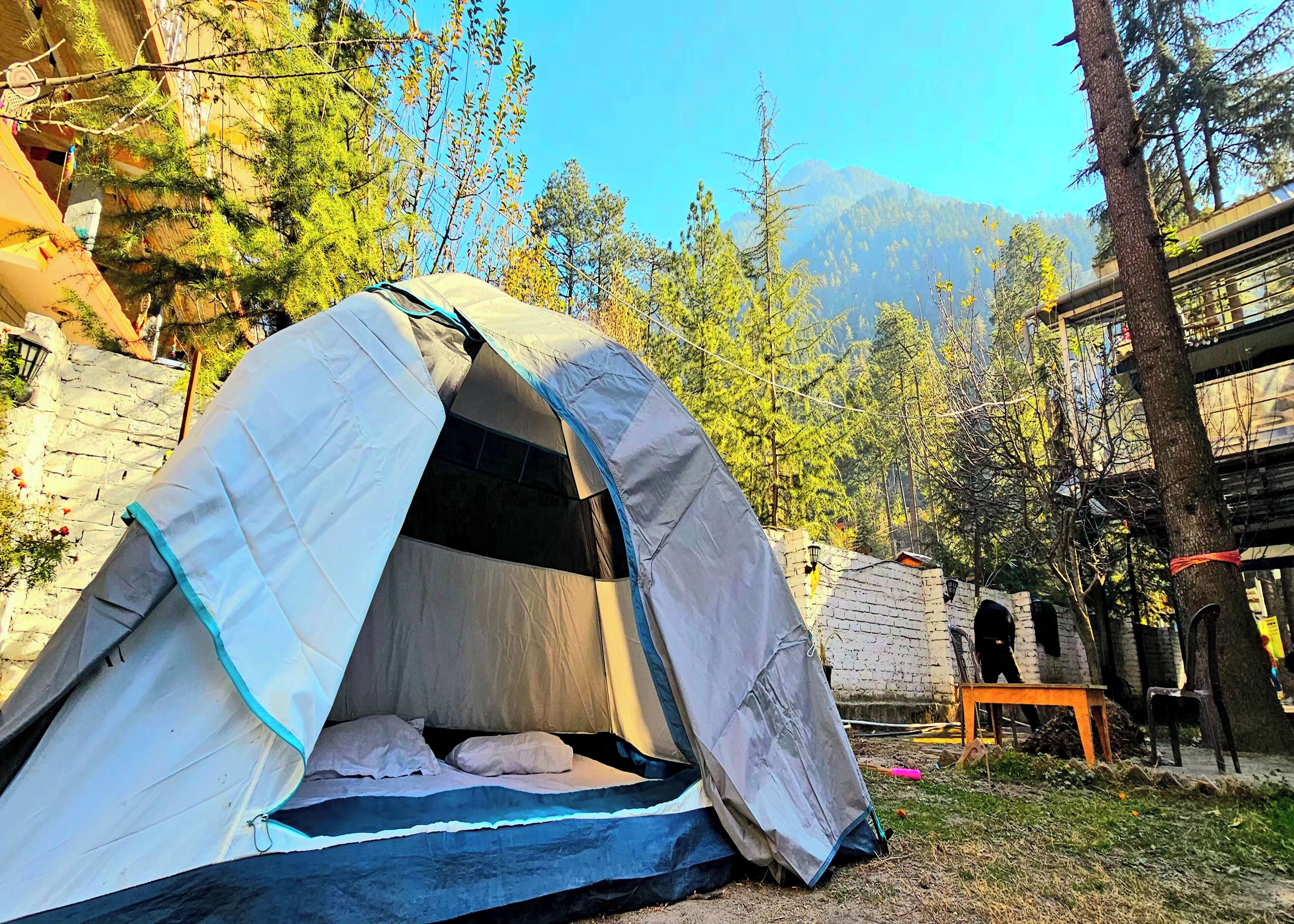 A tent set up in a natural environment with trees and a mountain in the background.