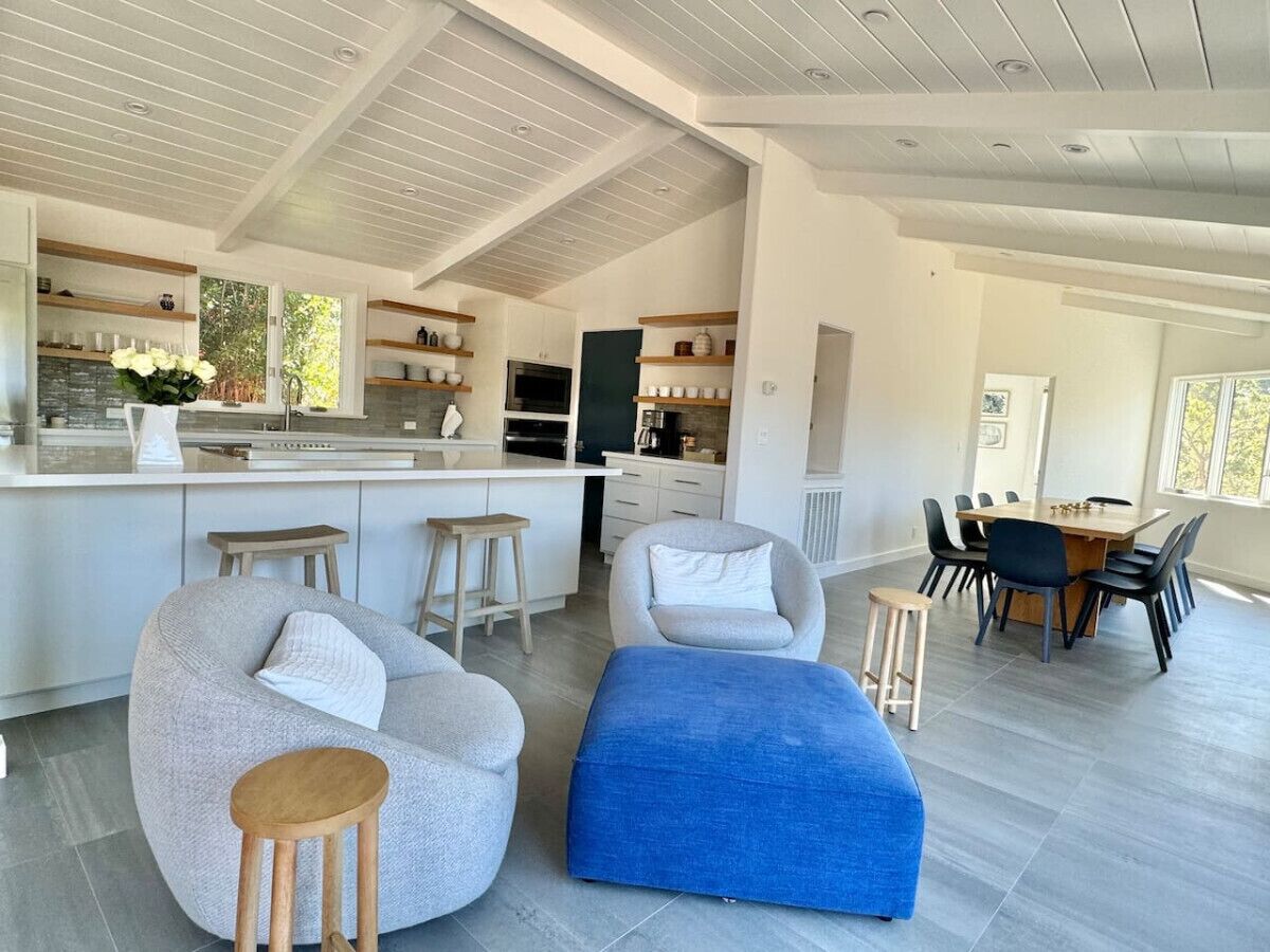 A modern kitchen with white cabinetry, a central island, and a dining area with a wooden table and chairs.