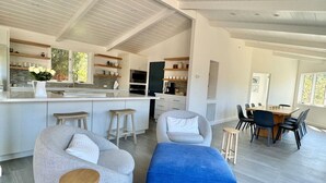 Uma cozinha moderna com armários brancos, uma ilha central e um espaço de refeições com mesa e cadeiras de madeira.