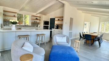 A modern kitchen with white cabinetry, a central island, and a dining area with a wooden table and chairs.