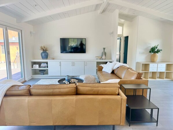 A modern living room with a large sofa, a coffee table, and a flat-screen TV mounted on the wall. - Point of Views - An Absolute Gem! (Point Reyes Station)