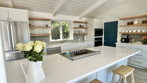 Cozinha moderna com armários brancos, uma ilha grande com bancos e um vaso de flores.