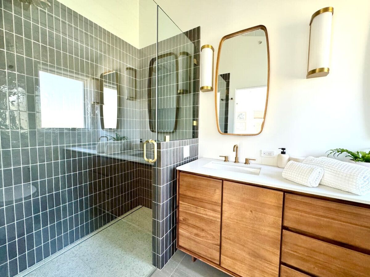 A modern bathroom with a glass shower enclosure, a wooden vanity, and a large mirror.