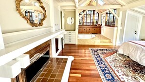 Une pièce spacieuse avec une cheminée, un grand miroir, un plancher en bois et une vue par la fenêtre.