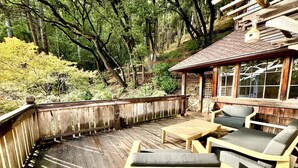 Une terrasse en bois, agrémentée de mobilier d’extérieur, entourée d’arbres et d’un mur de pierres.