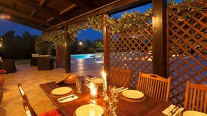 An outdoor dining area with a wooden table set for a meal, surrounded by wooden chairs, and a pool in the background. - Stunning villa with pool in the Marche countryside, just 10 minutes from the beaches of Senigallia (Senigallia)
