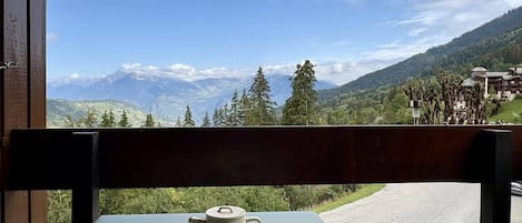 A table with a teapot and a mug, overlooking a mountainous landscape with a clear sky.