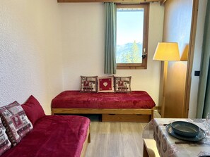 A bedroom with a bed, a wooden headboard, a window with a view of trees, a lamp, and a table with a plate and a glass.