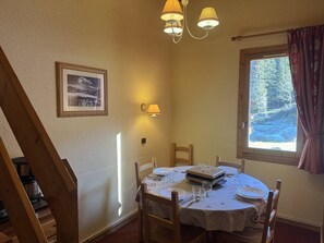 A dining area with a table set for four, a framed picture on the wall, and a window with a view of trees. - Lauzière Dessous 39 - Cosy 2-room apartment at the foot of the slopes (LES AVANCHERS VALMOREL)