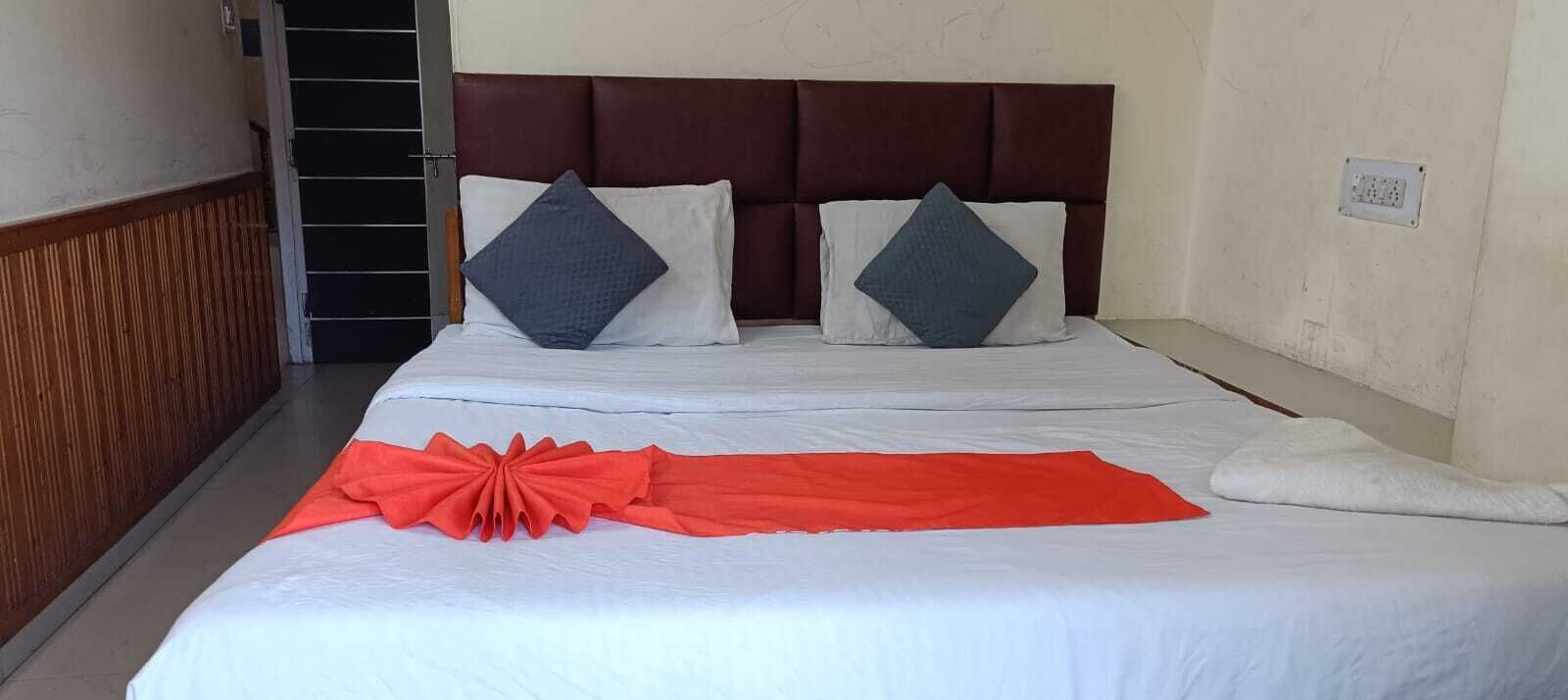 A double bed with white bedding and two pillows, a red decorative bow, and a wooden panel on the left.