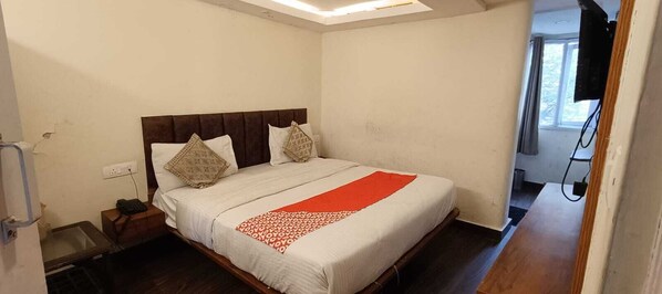 A bedroom with a bed, a nightstand, a TV, and a window.