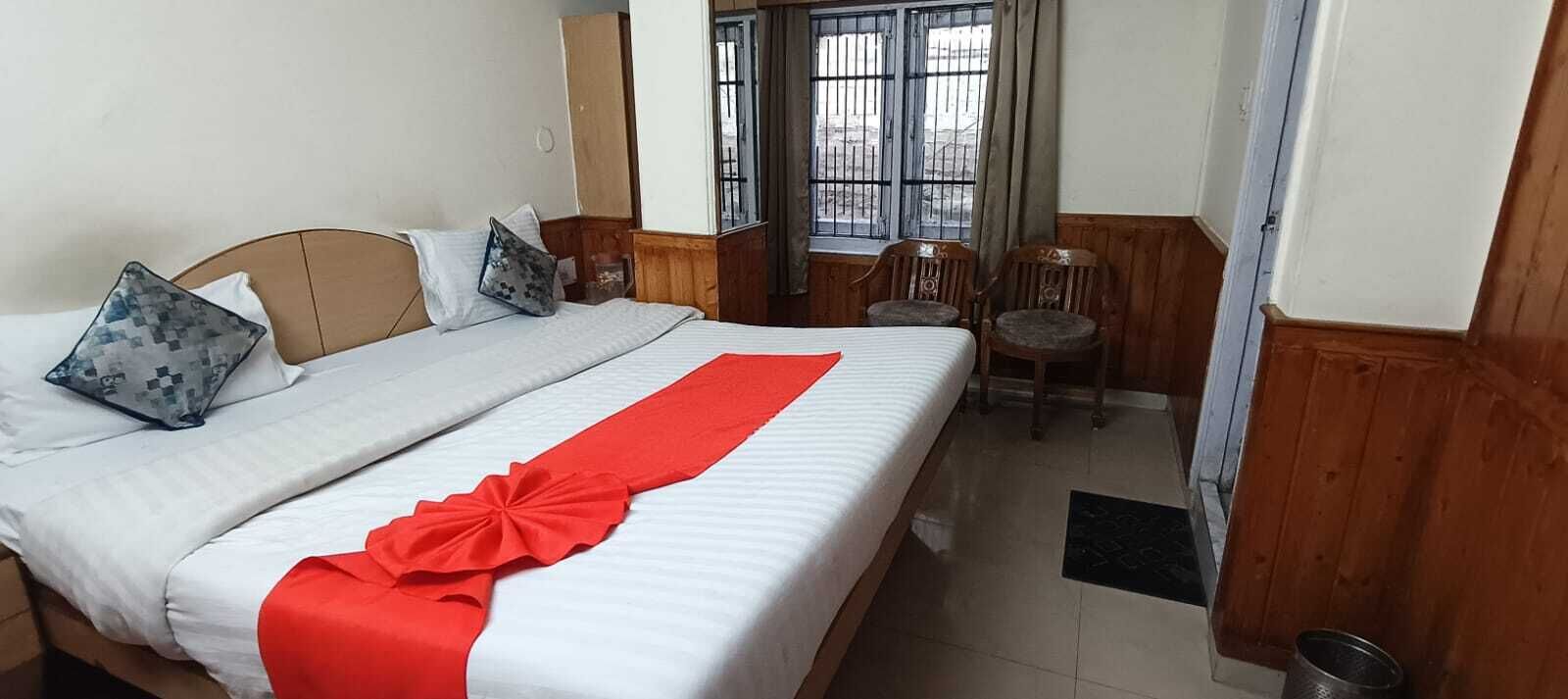 Habitación de hotel con cama, dos sillas, una ventana con rejas y una puerta.