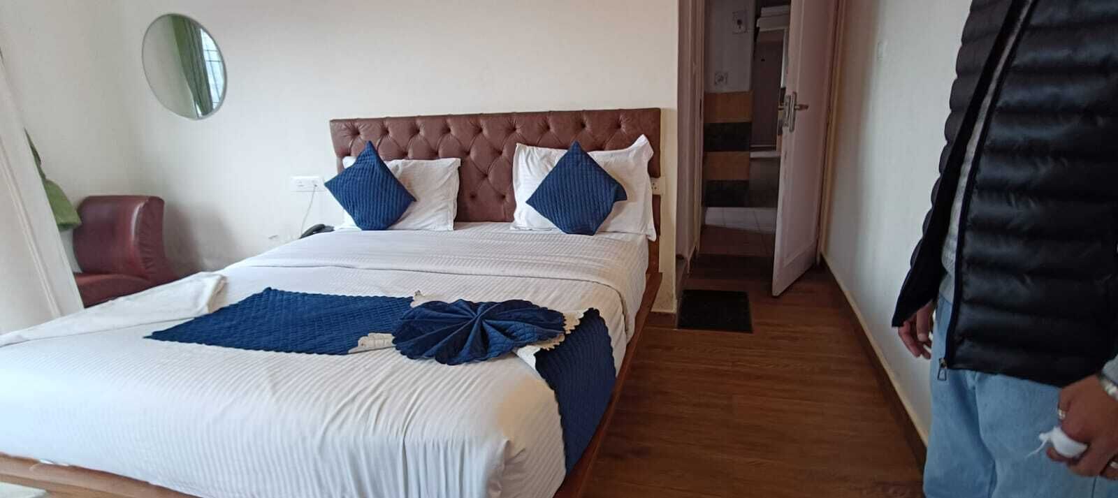 Habitación de hotel con una cama grande, cabecera marrón y un espejo en la pared.