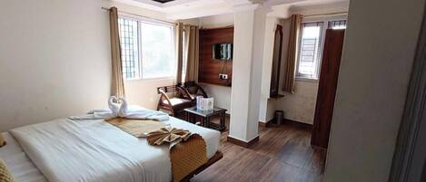 A hotel room with a large bed, a wooden chair, a small table, and a TV mounted on the wall.