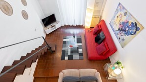 A modern living room with a staircase, a red sofa, a striped sofa, a flat-screen TV, and a painting on the wall. - Designer two-level apartment in the heart of Trastevere (Roma)