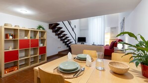 A dining area with a wooden table set for four, surrounded by red and wooden cabinets, a staircase, and a living room in the background. - Designer two-level apartment in the heart of Trastevere (Roma)